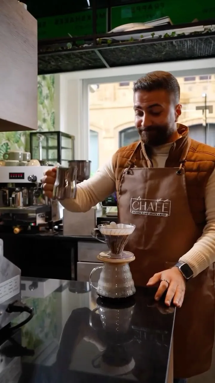 The barista brewing a V60 in a leather apron