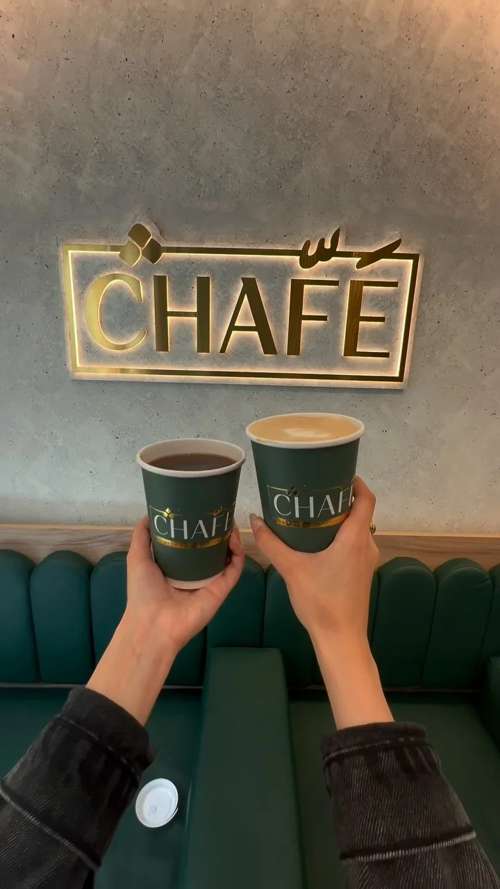 Two green CHAFÉ cups raised under the gold sign